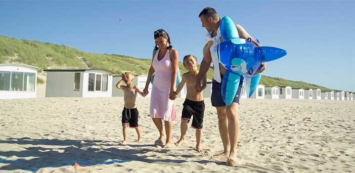 Mor og far går hånd i hånd med deres to drenge på stranden. Far har et stort badedyr under armen