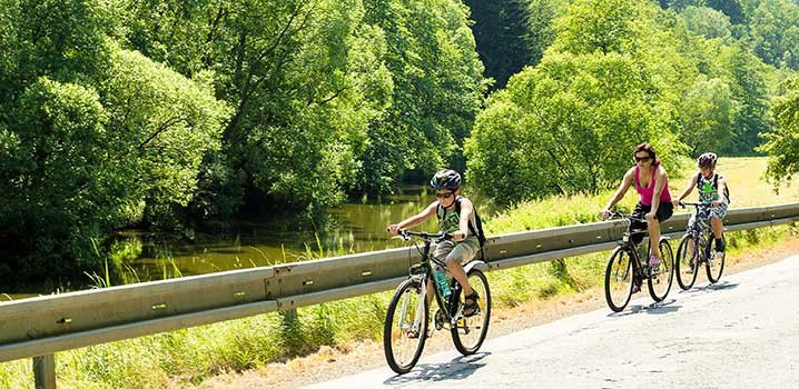 Mor og datter cykler på sti med buskads i baggrunden